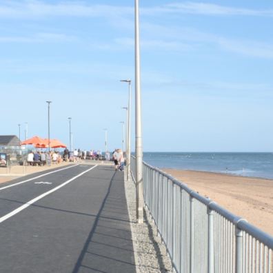 Resurfaced path in front of Sideshore, with the beach to the right and blue sky above